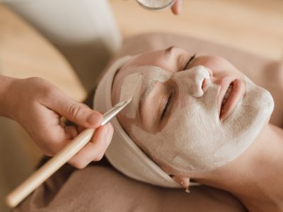 Mujer disfrutando de un masaje facial con crema aplicada con un pincel